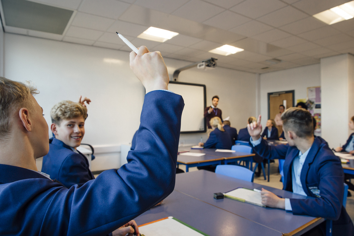A secondary school classroom, a student has raised their hand to answer a question.